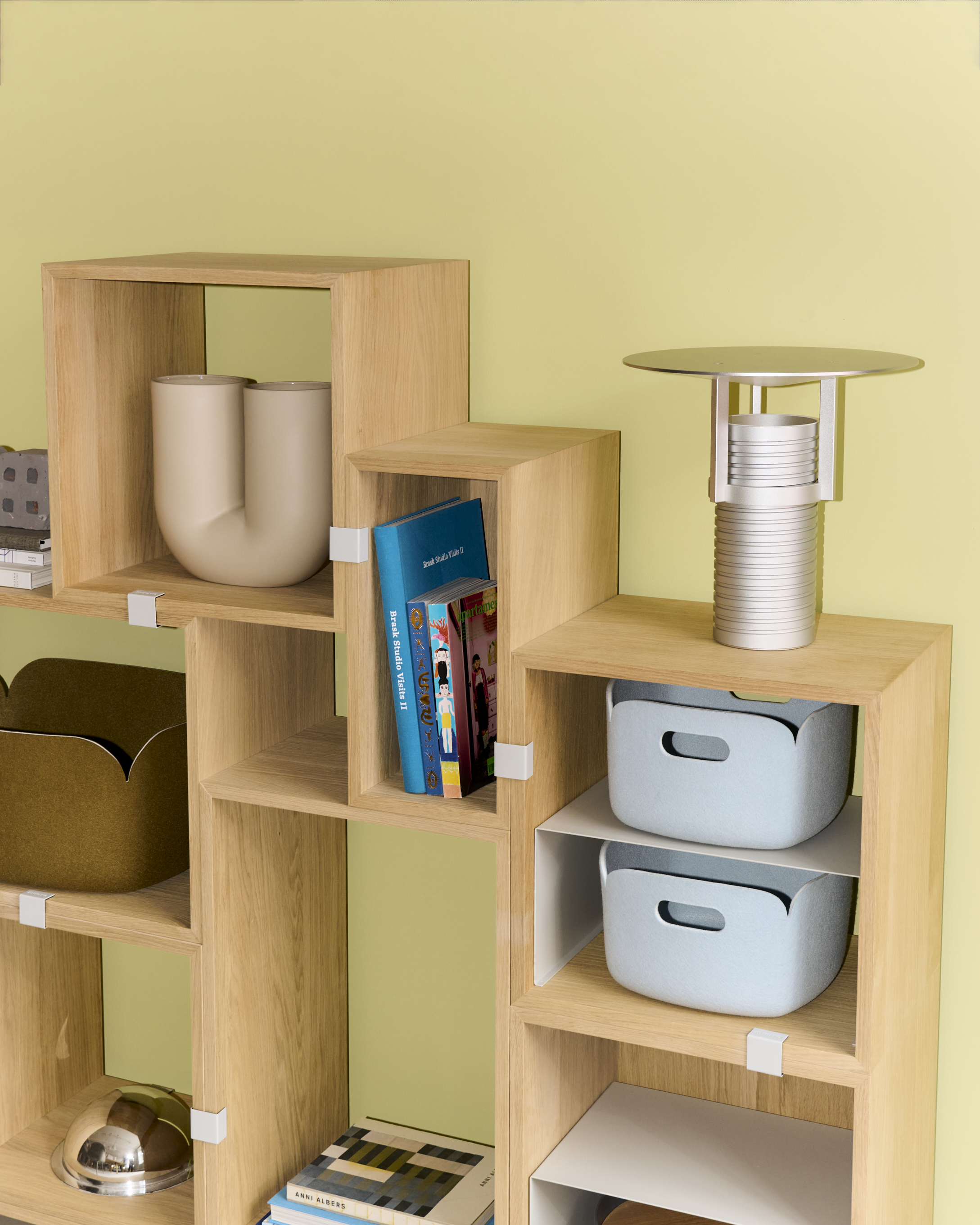 Image of the Muuto Restore Basket in Light Blue. The basket is part of a set placed on Stacked Bookcase in oak. A modern table lamp with a soft, rounded design complements the arrangement, creating a harmonious, minimalist aesthetic. The basket's recycled felt material adds a sustainable and functional element to the scene.