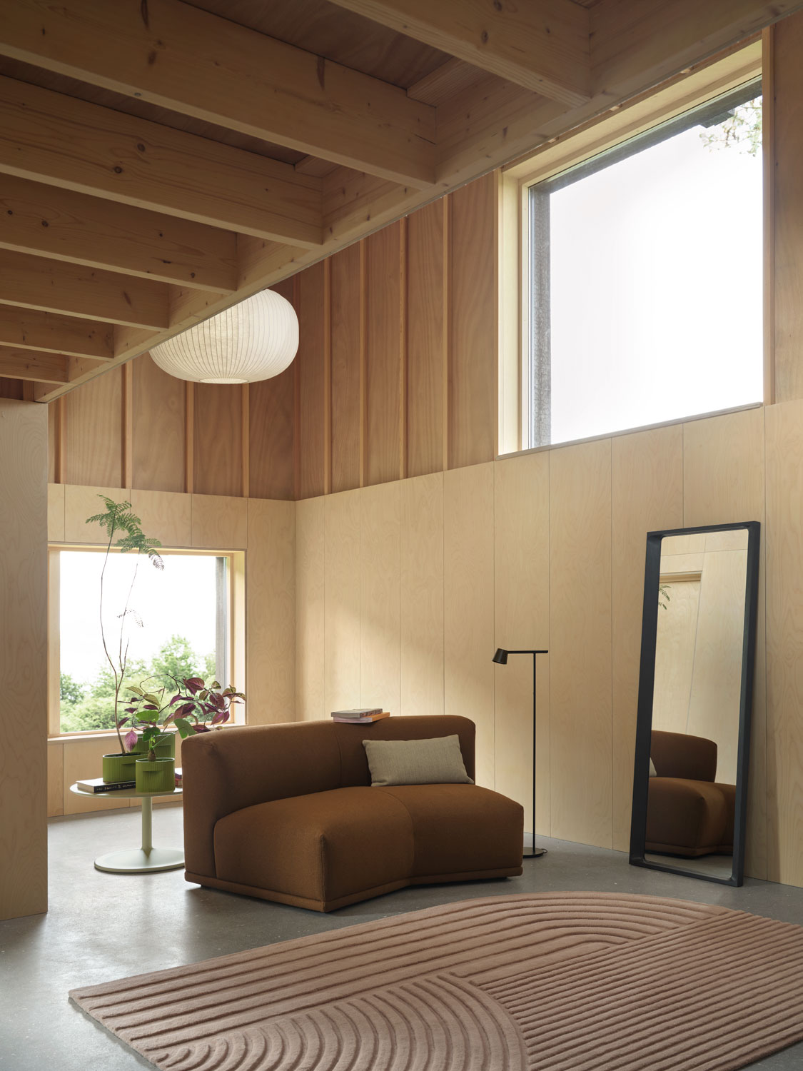 A modern living room by Muuto featuring a midnight blue arced mirror, a light rose Relevo rug with a sculptural pattern, and a Ridge Planter 13, 15 and 24 cm in moss green with ridged texture. The setup includes a Connect modular sofa in acca 361 upholstery, creating a cozy and modern atmosphere. The scene is complemented by Muuto's minimalist Tip table lamp, adding soft lighting to the contemporary design.