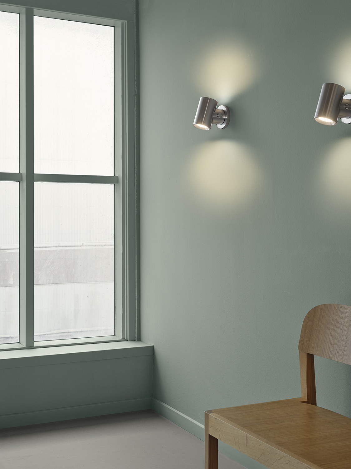 Two Beam Wall Lampa in polished aluminium casting a warm, comfortable light in a soft green room.