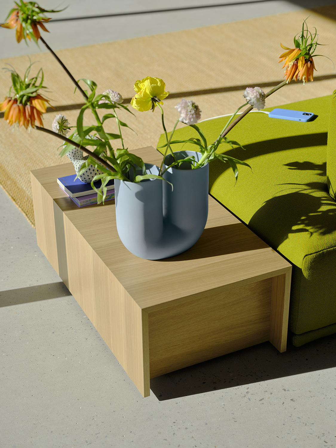 A Connect table in Oak Veneer placed in the sunlight and styled with a Kink Vase in light blue with orange and yellow flowers. 