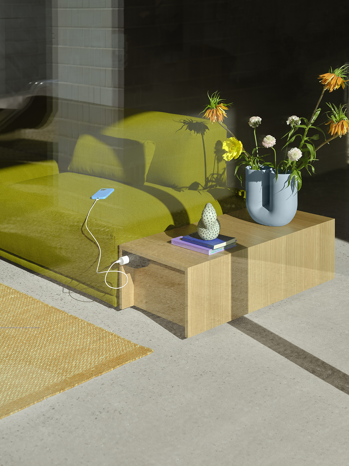 A Connect table in Oak Veneer and Connect Sofa placed in the sunlight and styled with a Kink Vase in light blue with orange and yellow flowers. 