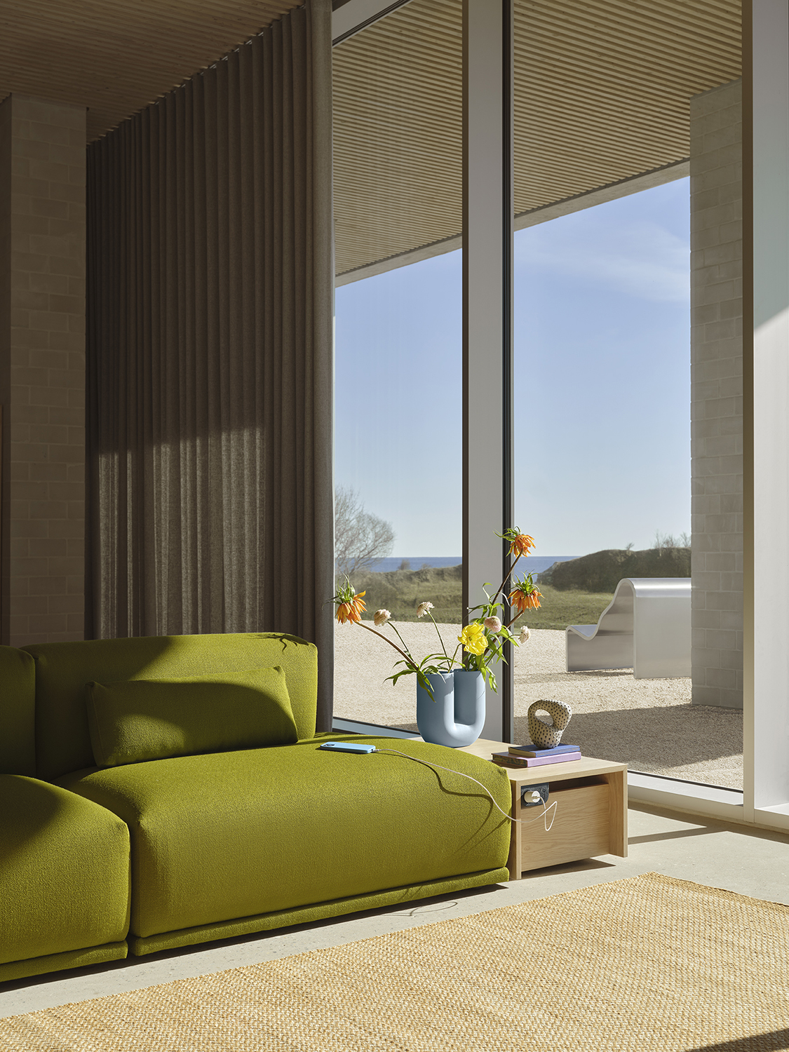 Connect Sofa and table placed on a Ply Rug in Burnt Orange. A Kink Vase in light blue with flowers is placed on the Connect table. 