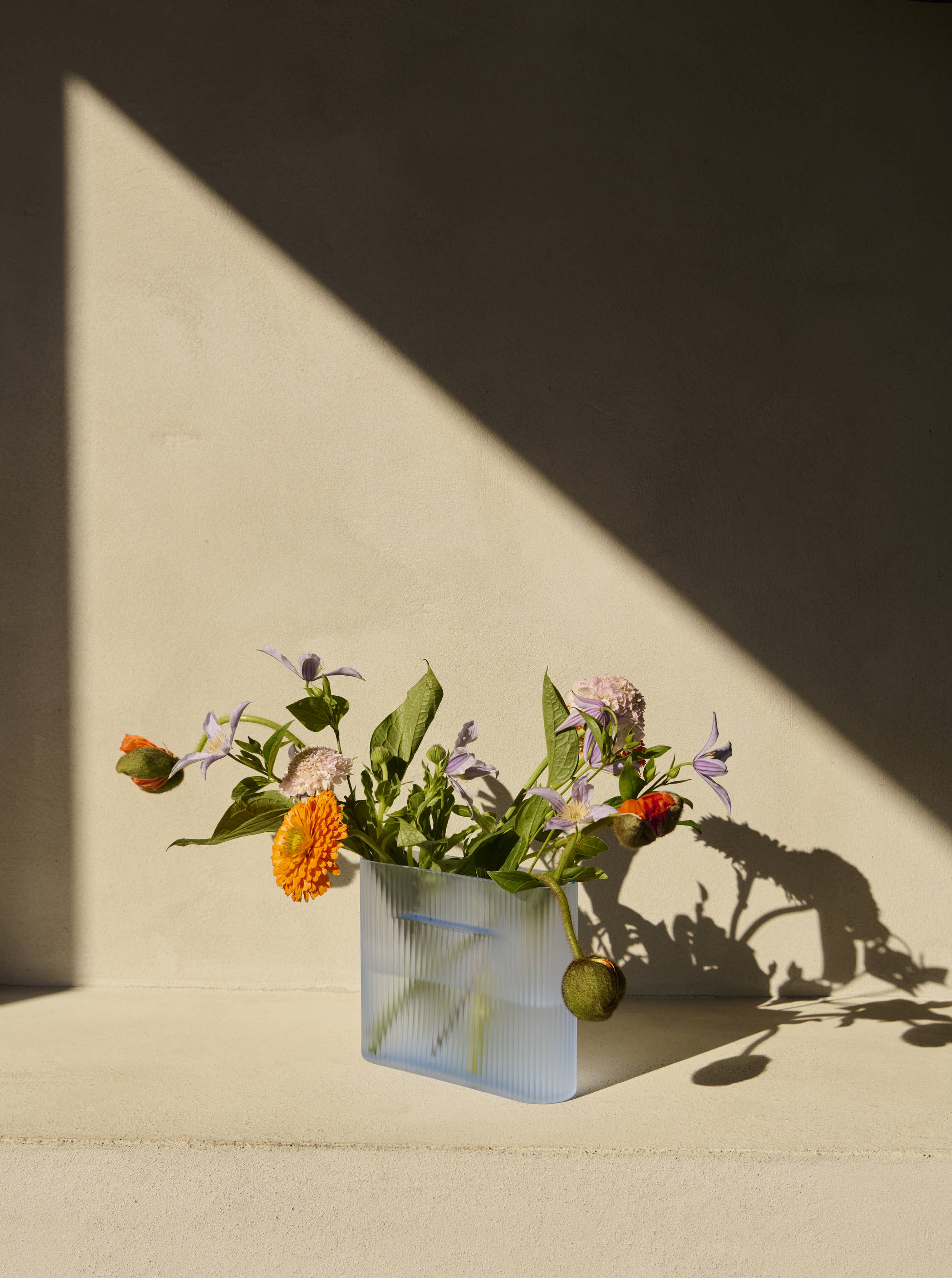 A modern, minimalistic vase in a light blue color, crafted from frosted glass and elegantly placed in the sunt to highlight its subtle design.